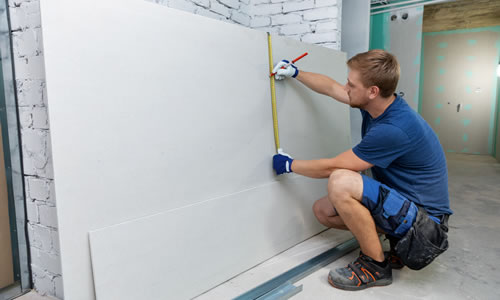 Man crouched down measuring plaster board
